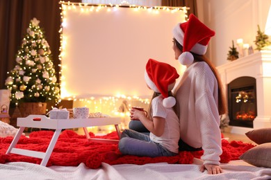 Photo of Mother and daughter watching movie using video projector at home. Cozy Christmas atmosphere