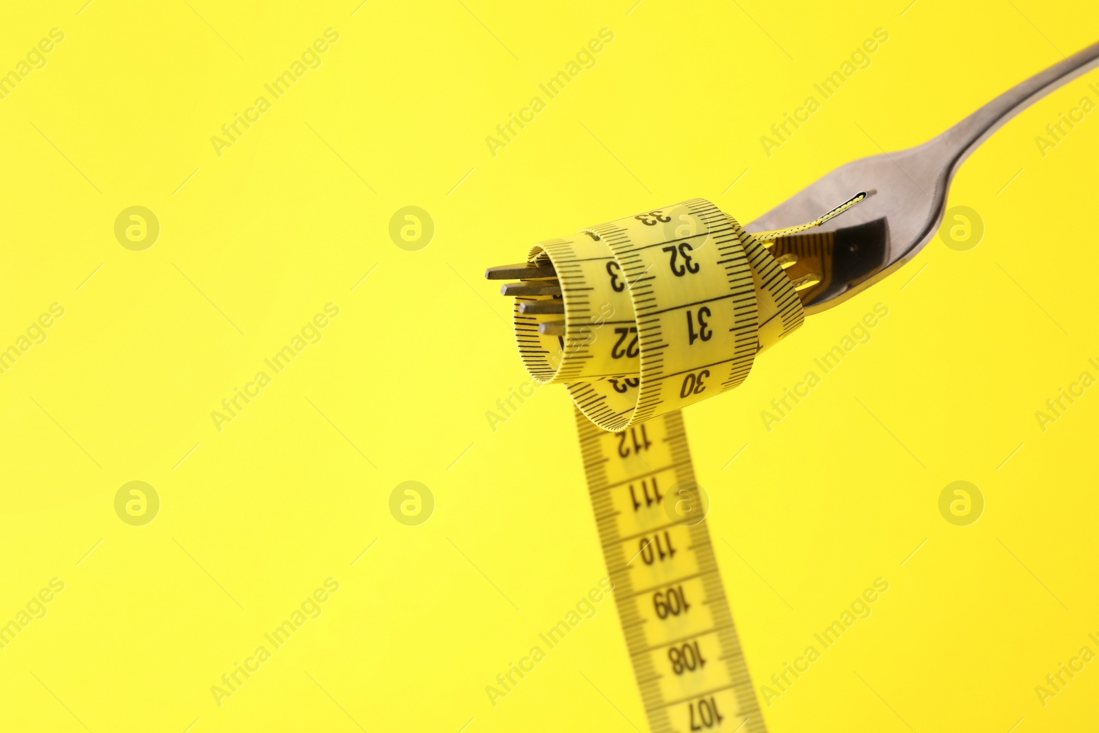 Photo of Fork with measuring tape on yellow background, space for text. Diet concept