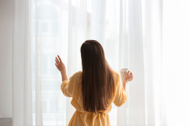 Photo of Young woman with cup near window indoors