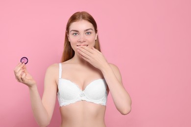Woman in bra holding condom on pink background, space for text. Safe sex