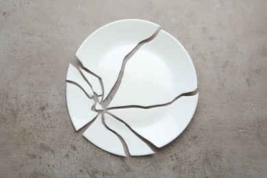 Photo of Pieces of broken ceramic plate on grey table, flat lay