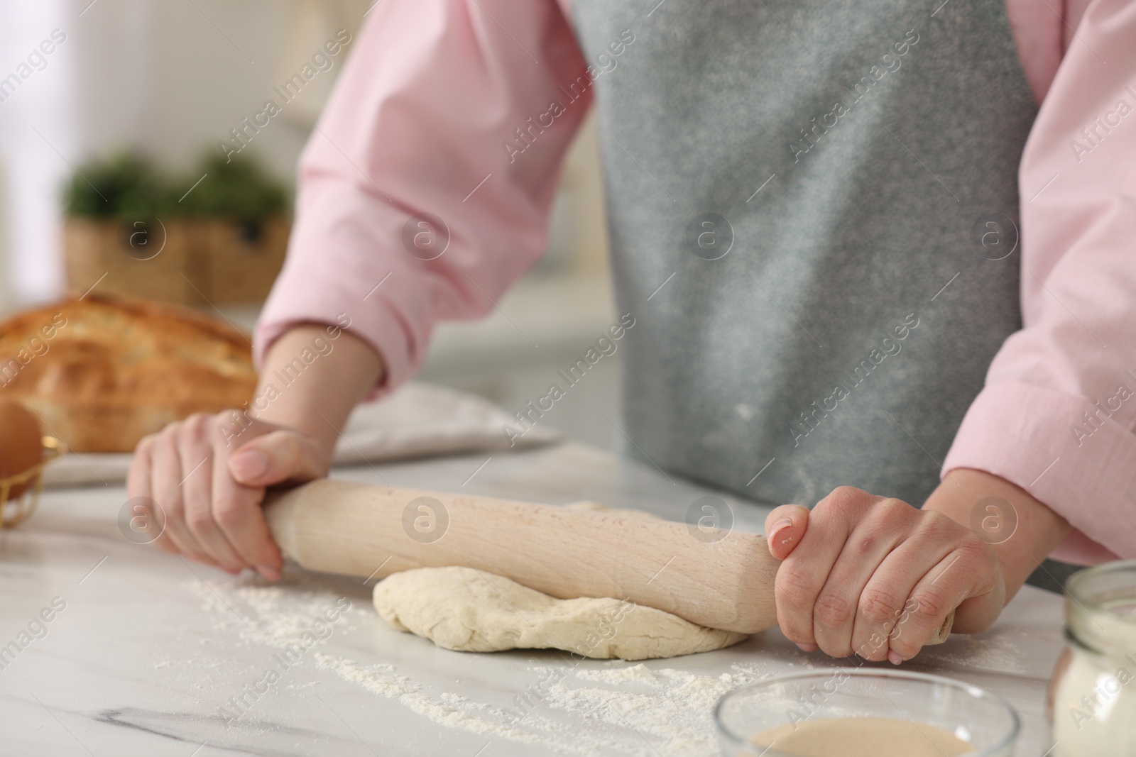 Photo of Making bread. Woman rolling raw dough at white table in kitchen, closeup