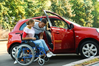 Young man helping disabled woman in wheelchair to get into car outdoors