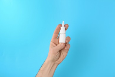 Photo of Man holding nasal spray on light blue background, closeup