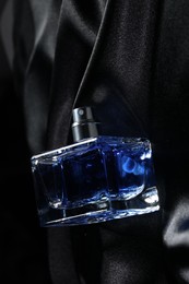 Photo of Luxury men's perfume in bottle on black satin fabric, top view