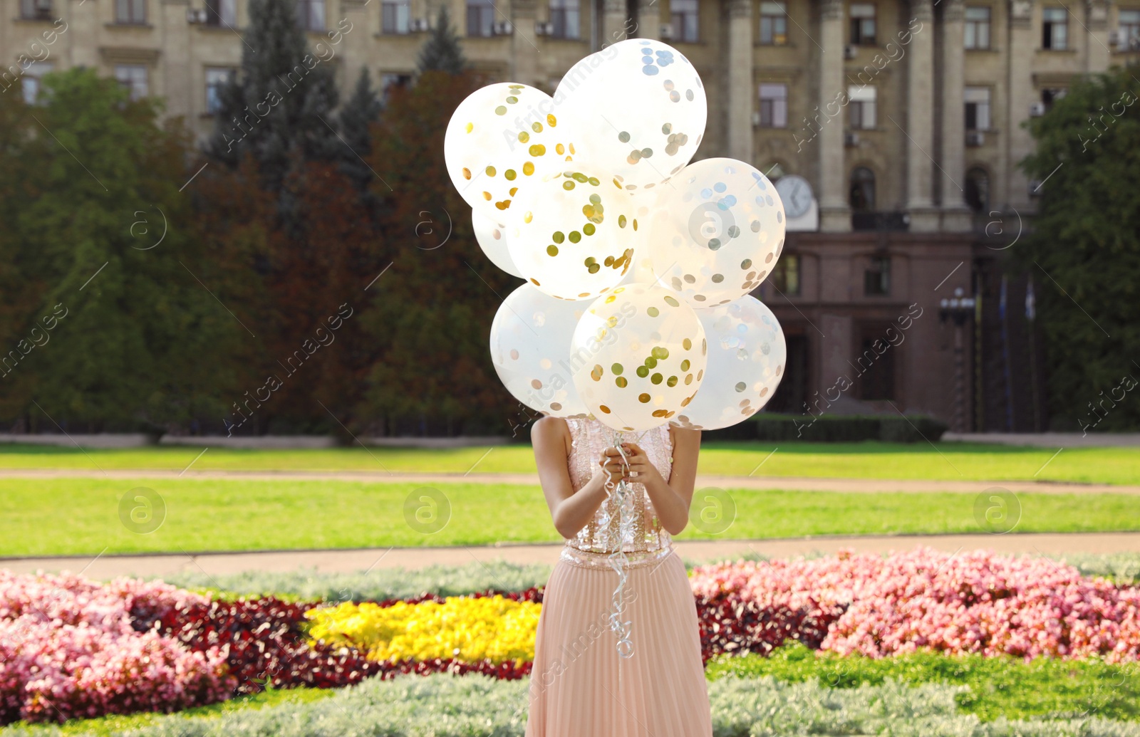 Photo of Young woman hiding behind glitter balloons on street