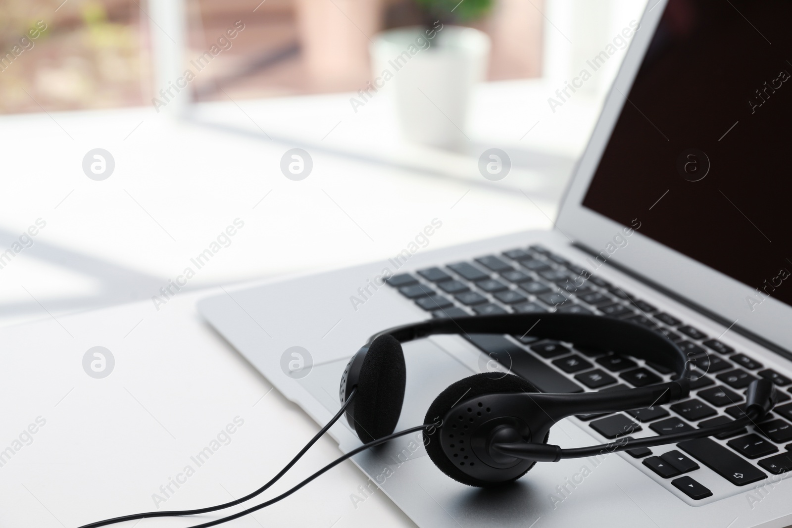 Photo of Modern laptop and headset on table indoors. Technical support concept