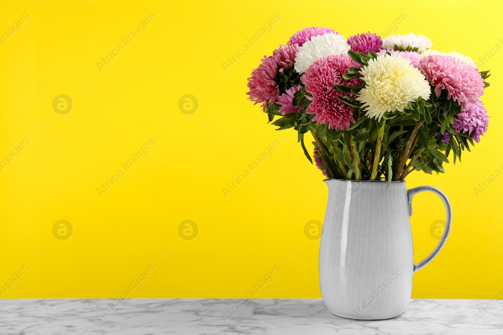 Photo of Beautiful asters in jug on table against yellow background, space for text. Autumn flowers