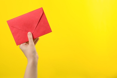 Woman holding red paper envelope on yellow background, closeup. Space for text