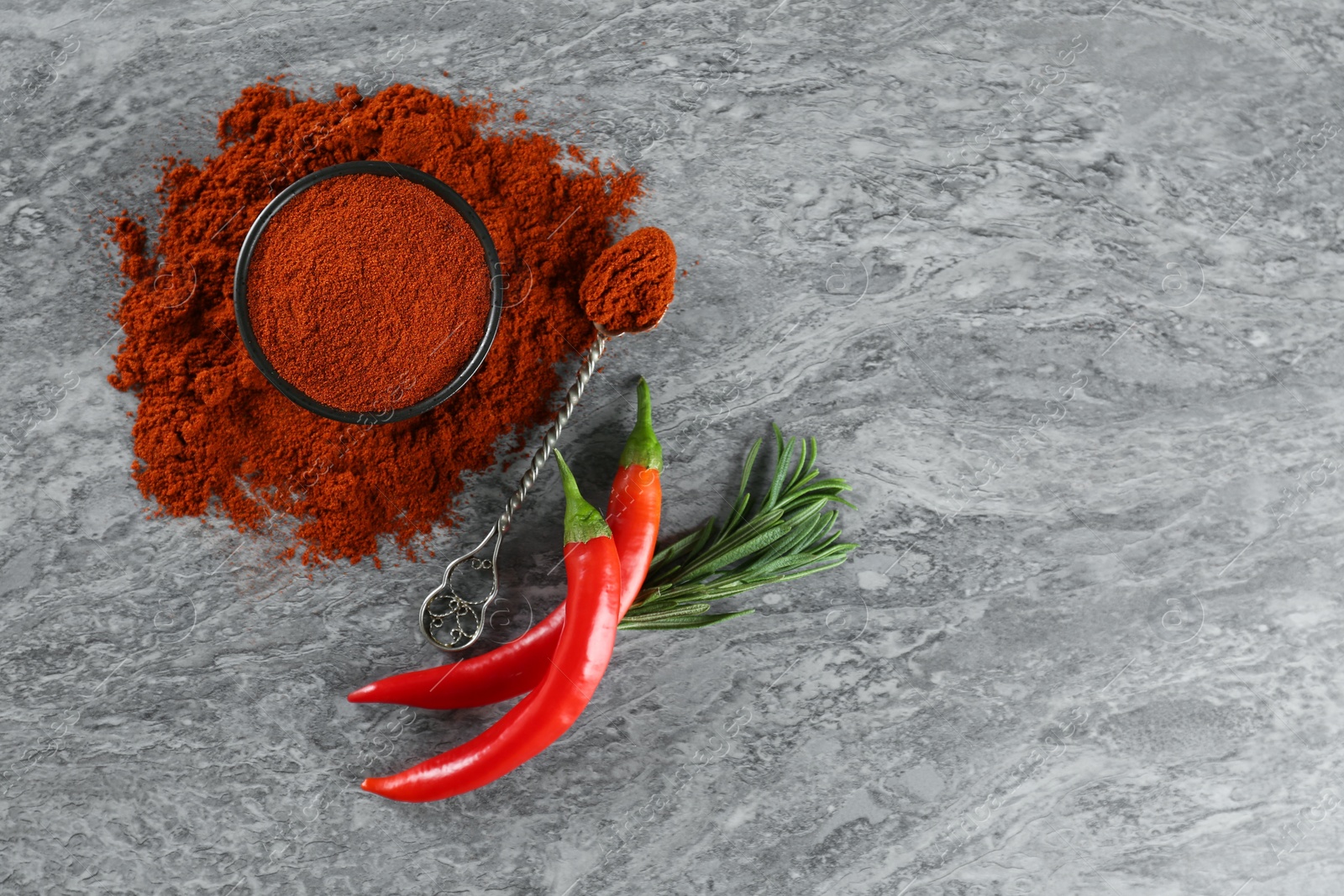 Photo of Ground red pepper with spoon and ingredients on grey marble table, flat lay. Space for text