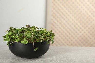 Fresh radish microgreens in bowl on light grey table, space for text