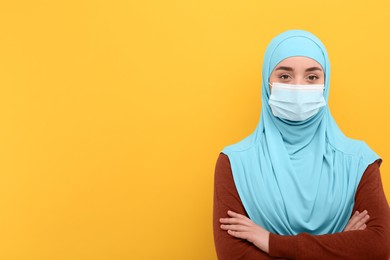 Portrait of Muslim woman in hijab and medical mask on orange background, space for text