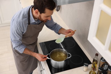 Photo of Man cooking delicious chicken soup in kitchen, above view