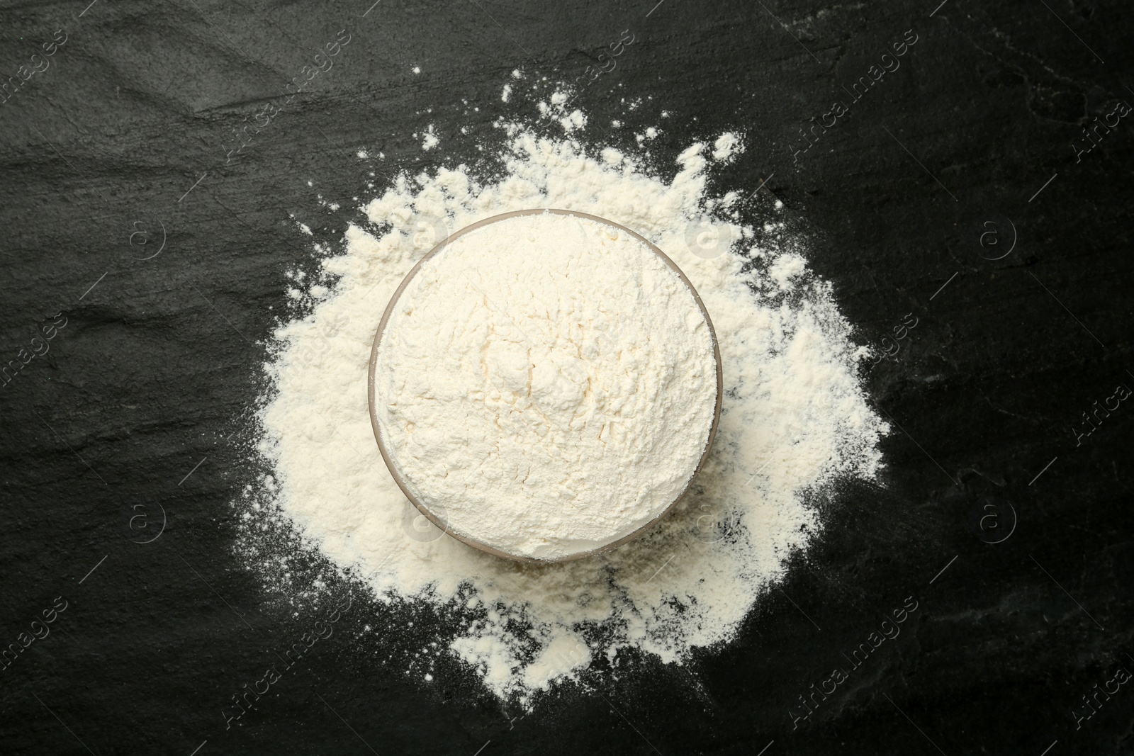 Photo of Ceramic bowl with flour on black table, flat lay. Cooking utensils