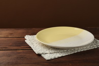 Photo of Beautiful ceramic plate and napkin on wooden table against brown background, space for text