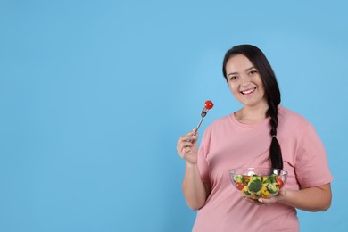 Photo of Beautiful overweight woman eating salad on light blue background, space for text. Healthy diet