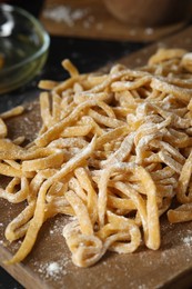 Photo of Board with homemade pasta and flour on dark table, closeup