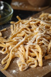 Board with homemade pasta and flour on dark table, closeup