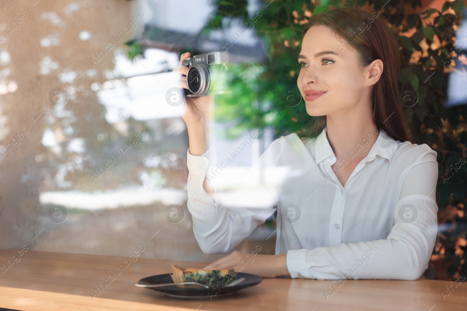 Photo of Young woman with camera taking photo at cafe, view through window. Creative hobby