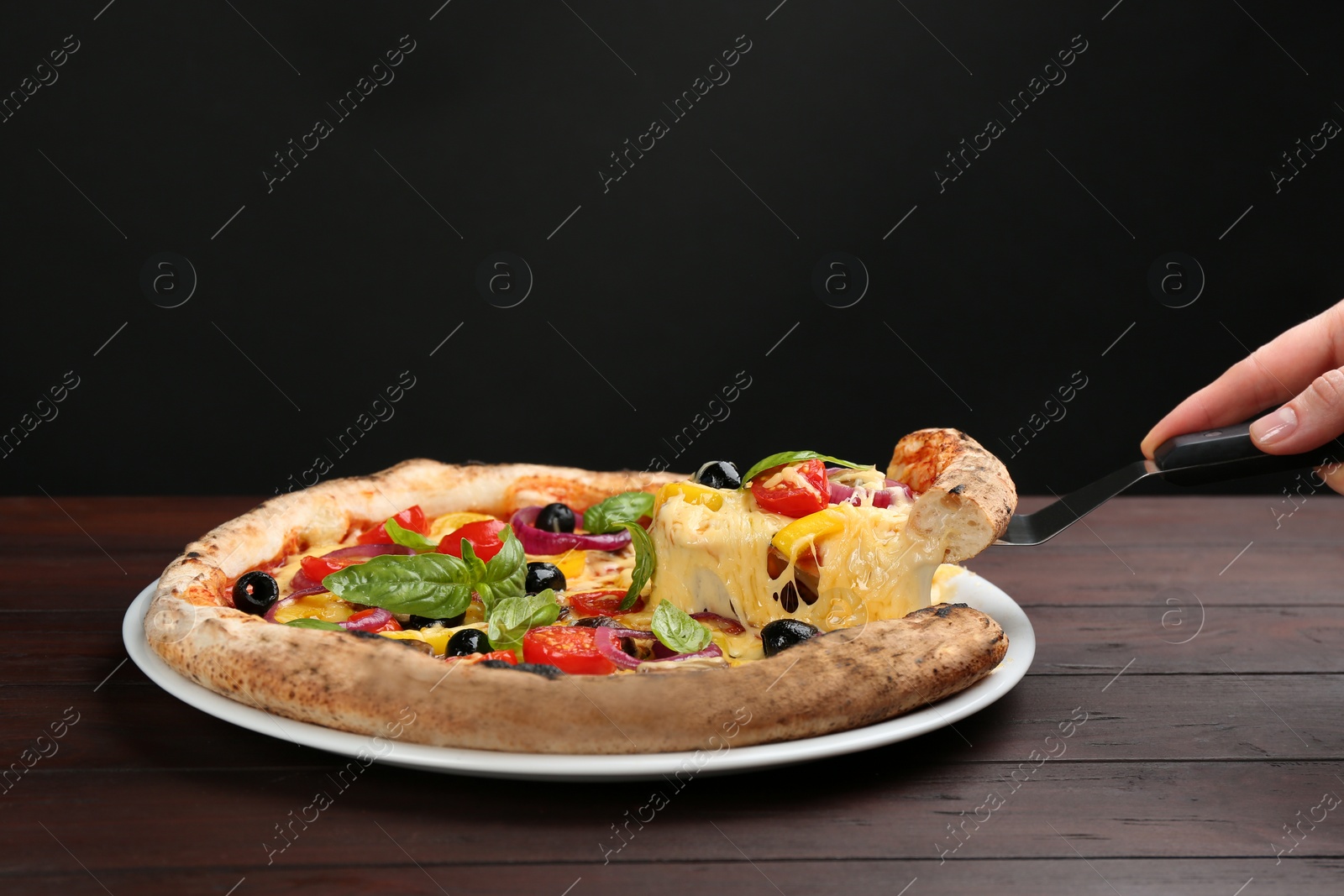 Photo of Woman taking slice of tasty vegetable pizza at wooden table, closeup