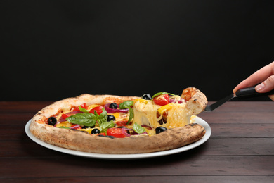 Woman taking slice of tasty vegetable pizza at wooden table, closeup