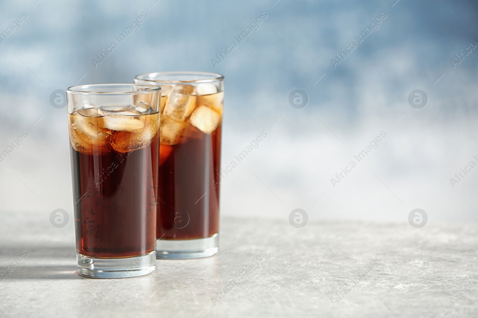 Photo of Glasses of cold cola on table against color background. Space for text