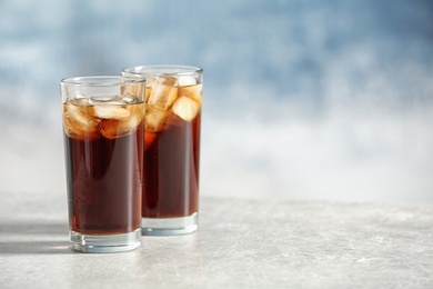 Glasses of cold cola on table against color background. Space for text