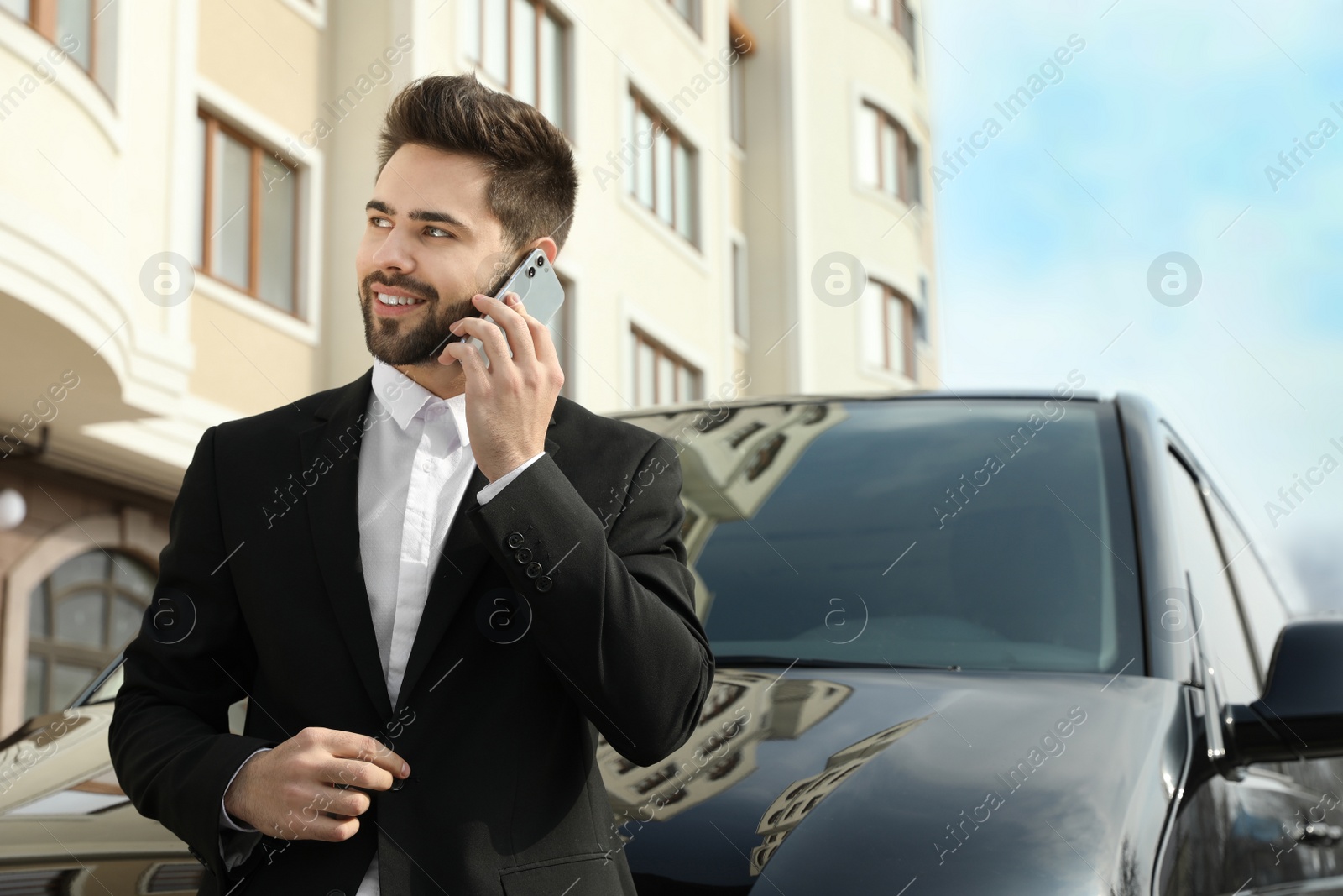 Photo of Handsome man talking on smartphone near modern car outdoors