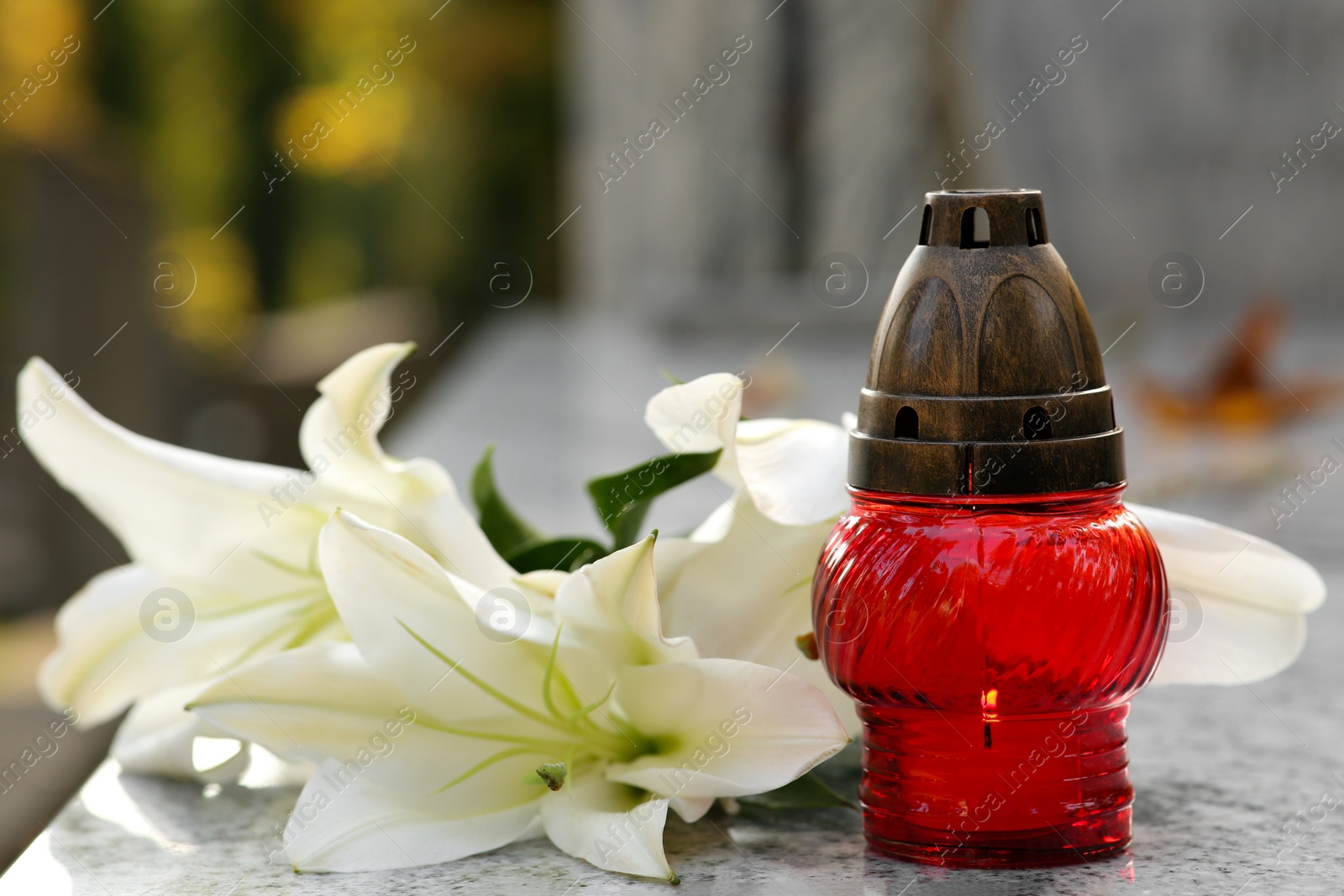 Photo of White lilies and grave lantern on granite tombstone outdoors. Funeral ceremony