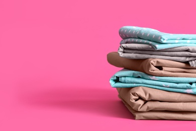 Photo of Stack of clean bed sheets on pink background. Space for text