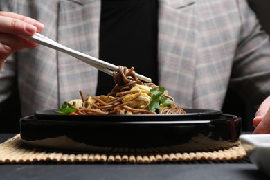 Photo of Stir-fry. Woman eating tasty noodles with meat and vegetables at dark table, closeup