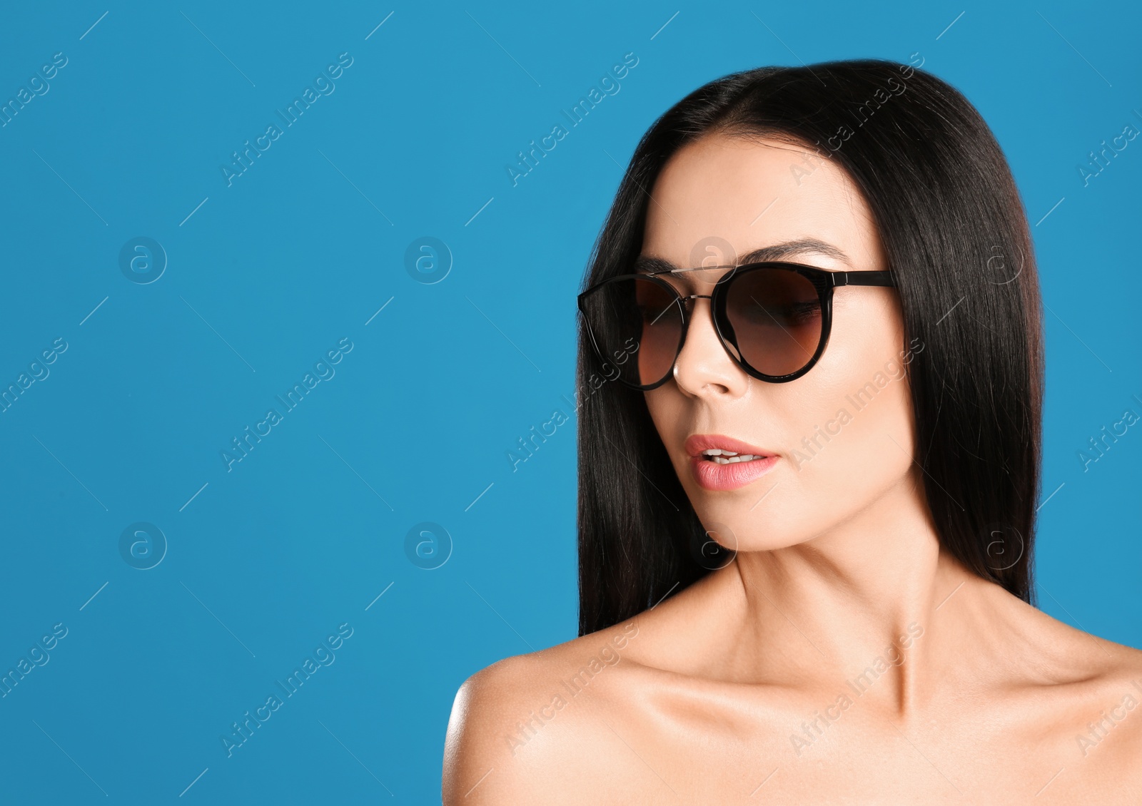 Photo of Beautiful woman wearing sunglasses on blue background, closeup. Space for text
