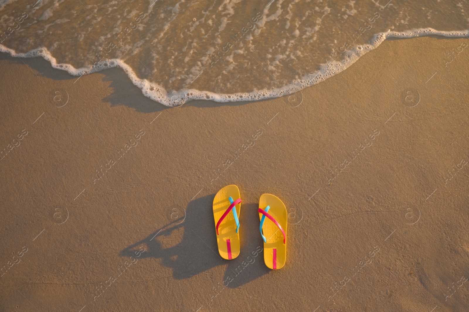 Photo of Bright yellow beach slippers on sand near sea, top view. Space for text