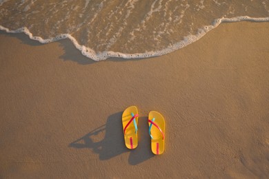 Bright yellow beach slippers on sand near sea, top view. Space for text