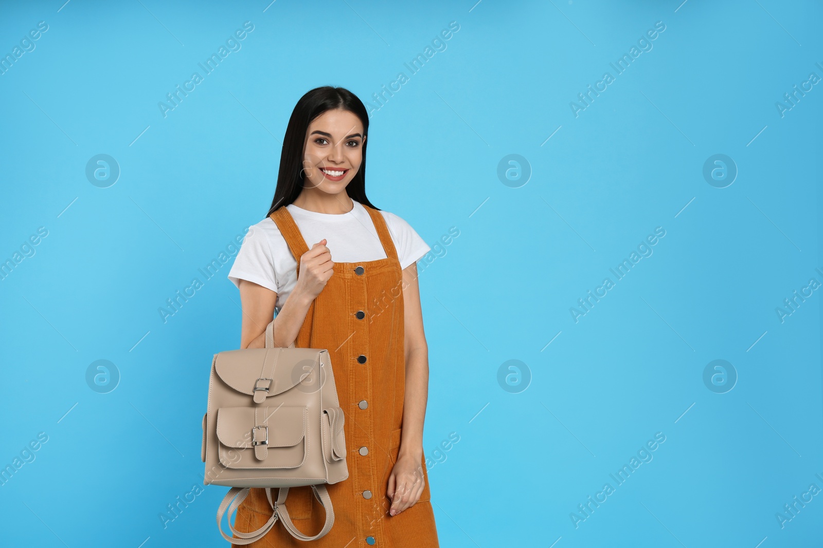 Photo of Young woman with stylish backpack on light blue background. Space for text