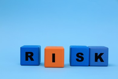 Photo of Color wooden cubes with word Risk on light blue background