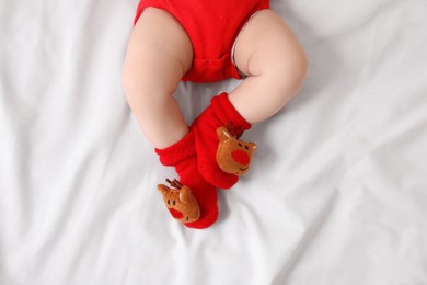 Photo of Baby wearing festive Christmas socks on white bedsheet, top view