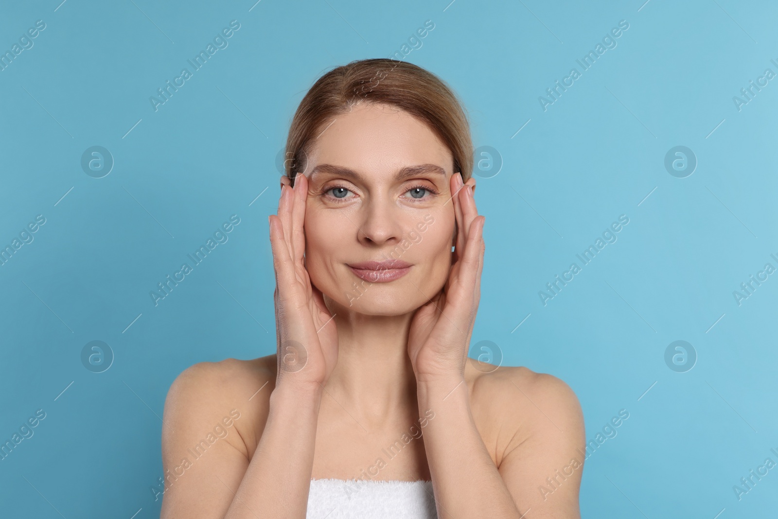 Photo of Woman massaging her face on turquoise background