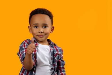 Photo of African-American boy showing thumb up on orange background. Space for text