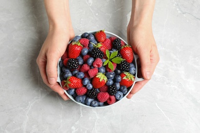 Woman with bowl of delicious berries at light table, closeup