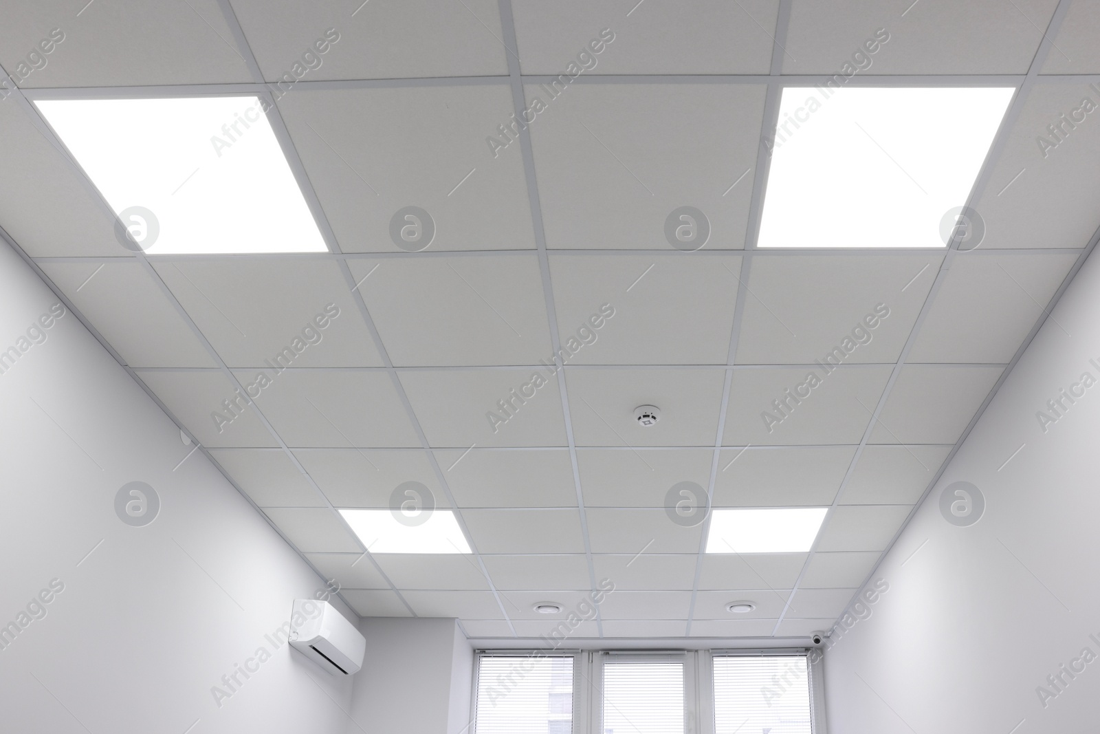 Photo of White ceiling with PVC tiles and lighting indoors, low angle view