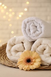 Photo of Rolled terry towels and flower on white table near brick wall indoors