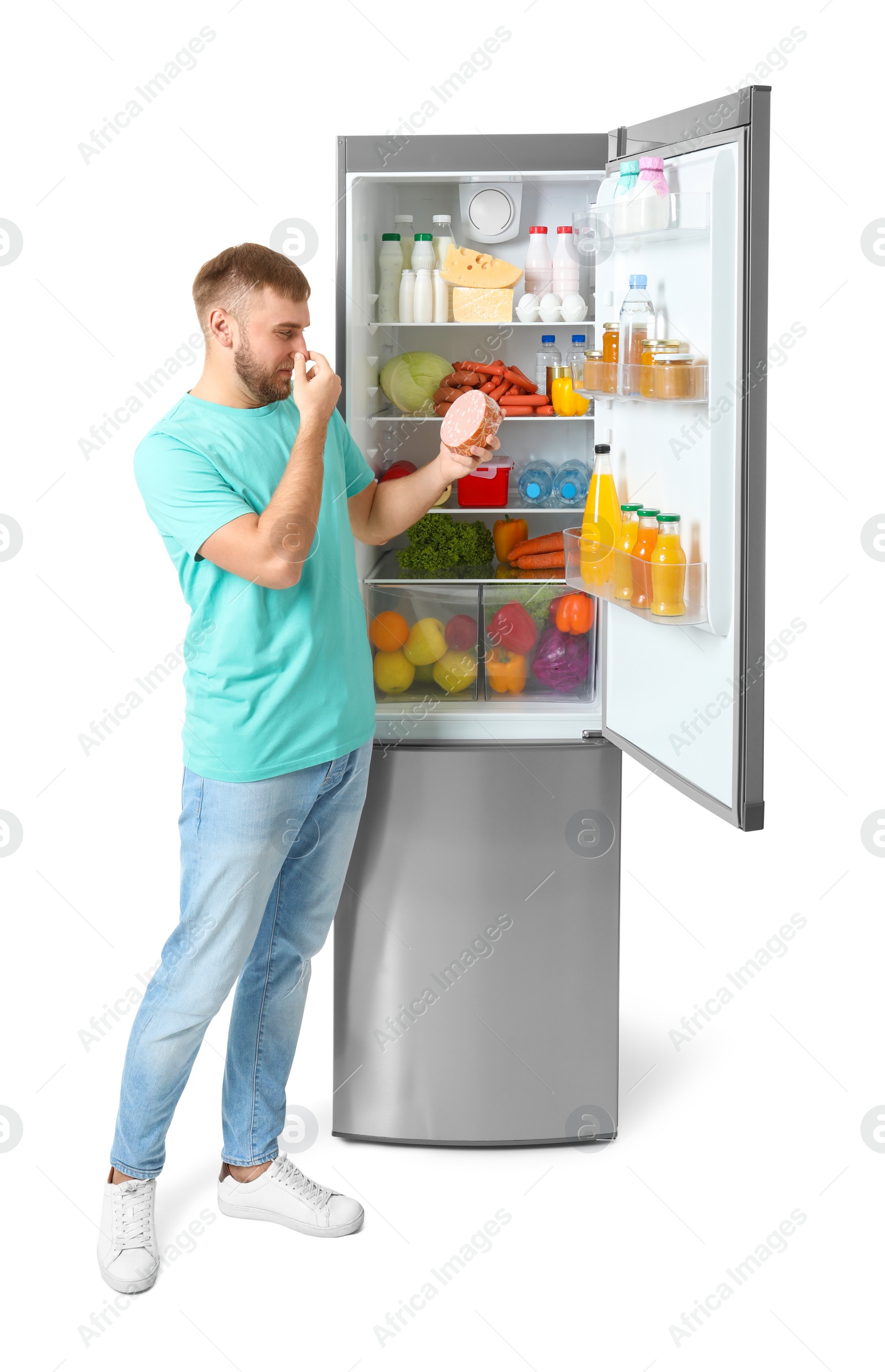 Photo of Young man with expired sausage near open refrigerator on white background