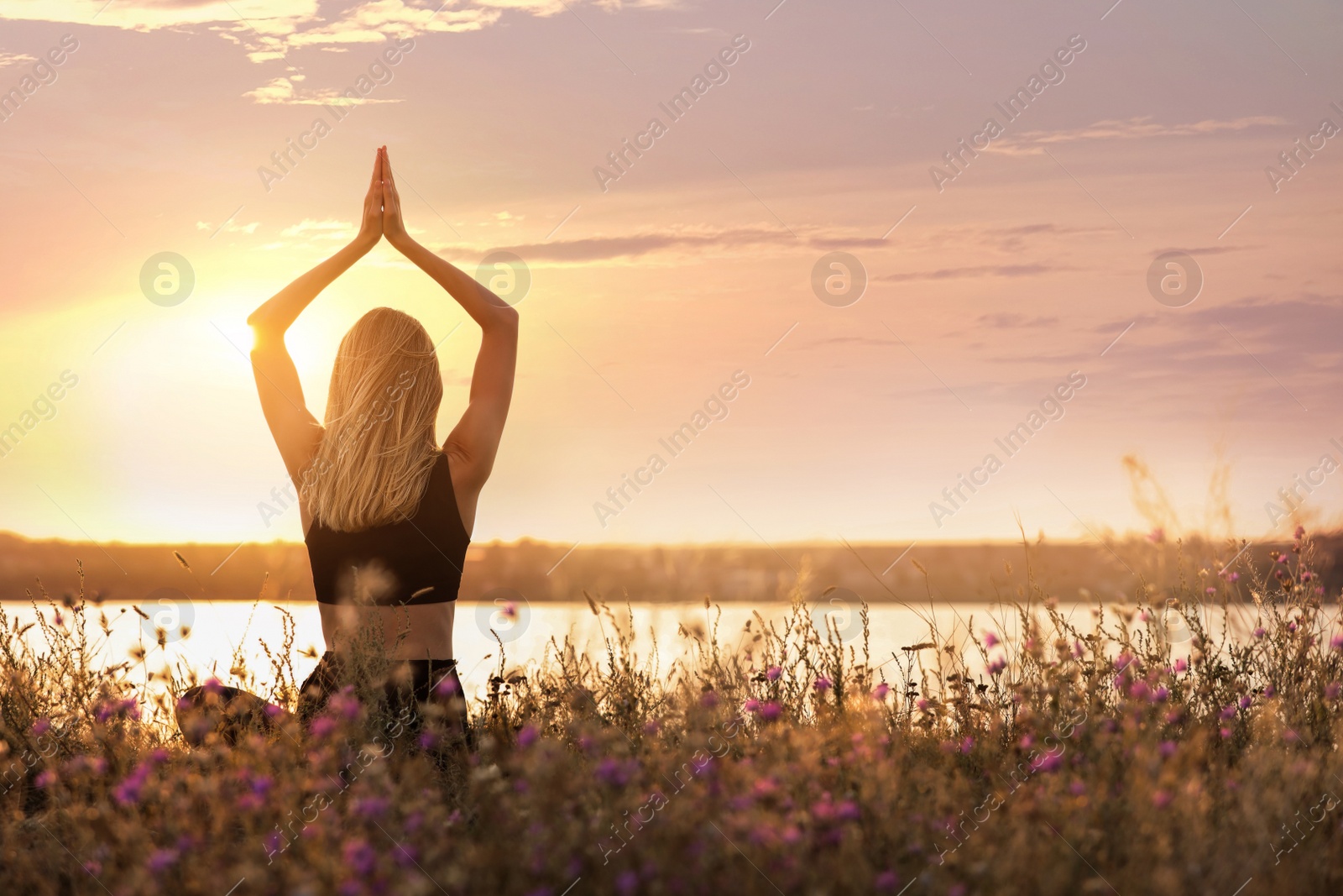 Image of Young woman meditating near river at sunrise, back view. Practicing yoga