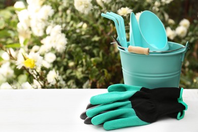 Gardening gloves and bucket with different tools on white wooden table outdoors, space for text