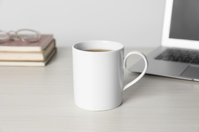 Photo of One ceramic mug with drink and laptop on white wooden table