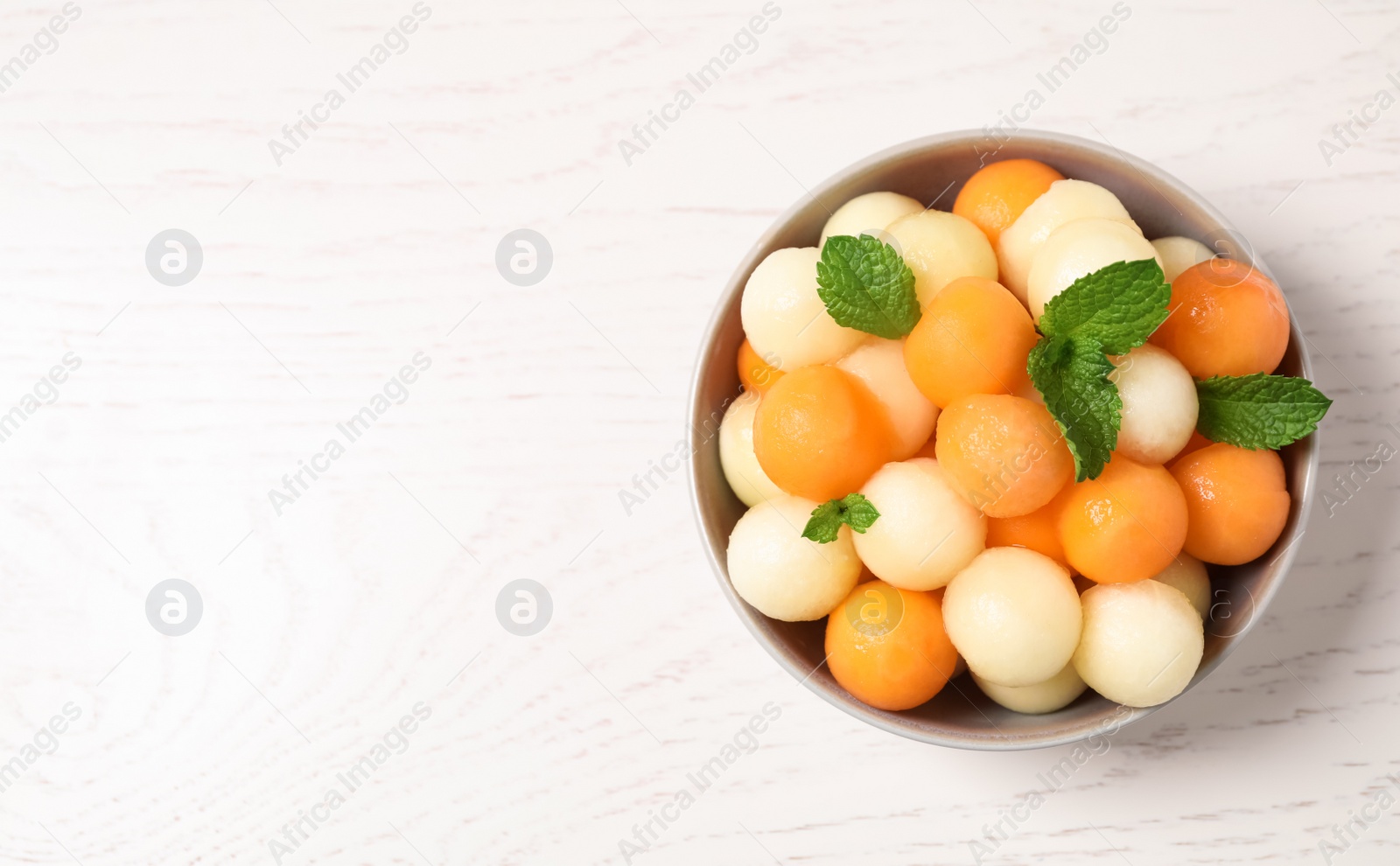 Photo of Melon balls and mint in bowl on white wooden table, top view. Space for text