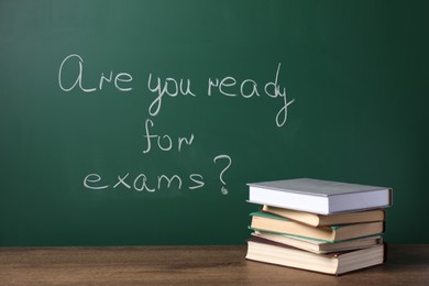 Books on wooden table near chalkboard with phrase Are You Ready For Exams