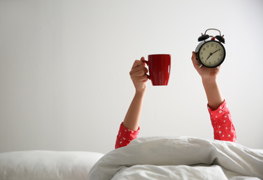 Photo of Closeup view of woman with cup and alarm clock lying in bed, space for text. Morning time