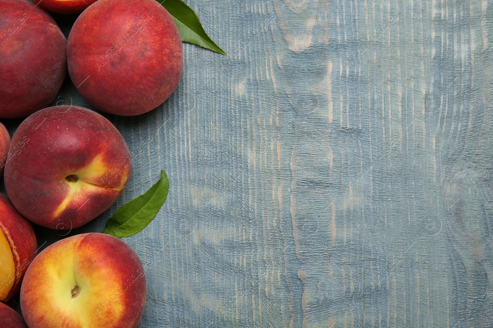 Photo of Fresh peaches and leaves on blue wooden table, top view with space for text